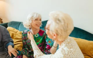 Two older women smiling and enjoying a conversation while seated together on a sofa.