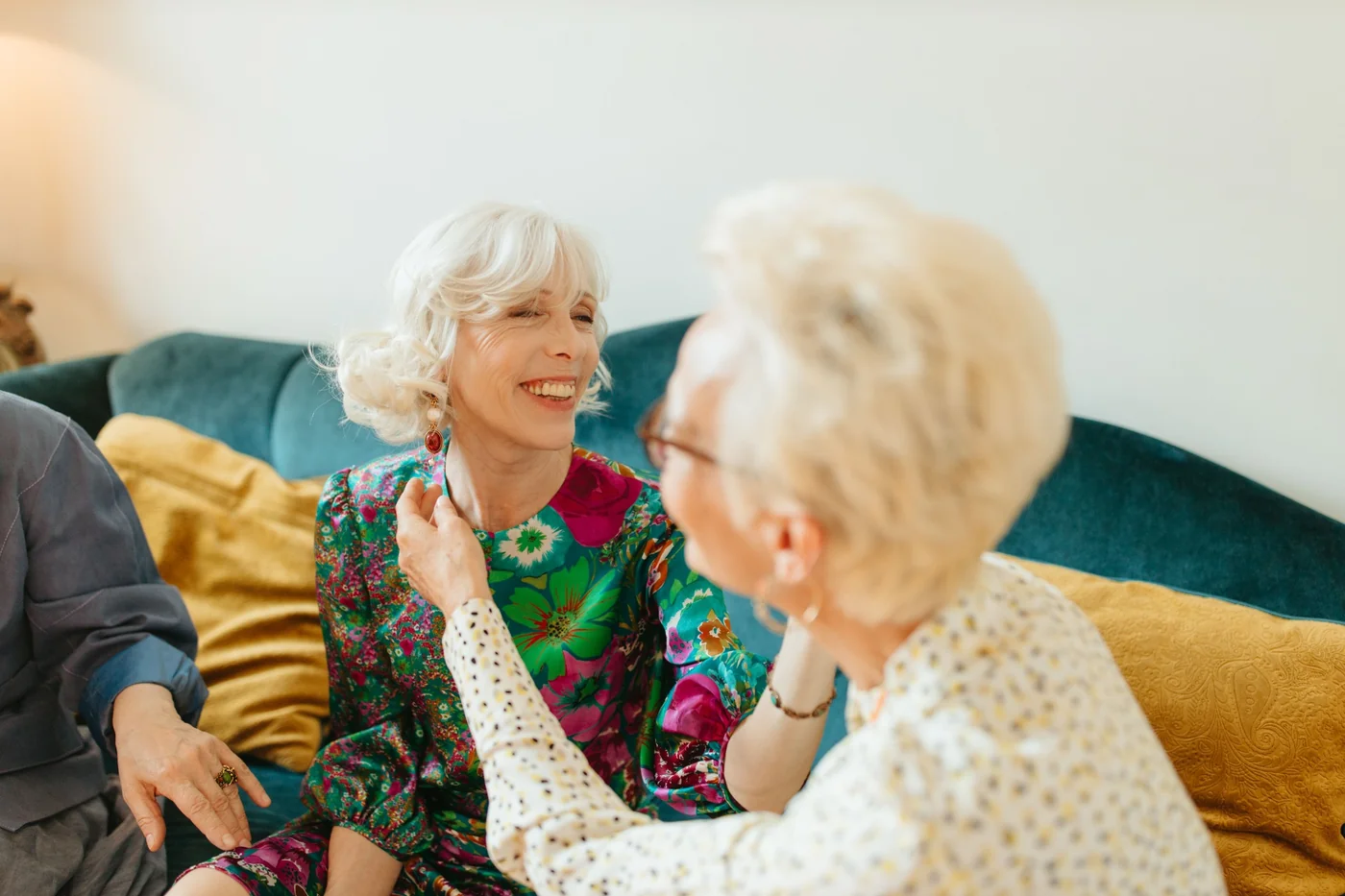 Two older women smiling and enjoying a conversation while seated together on a sofa.